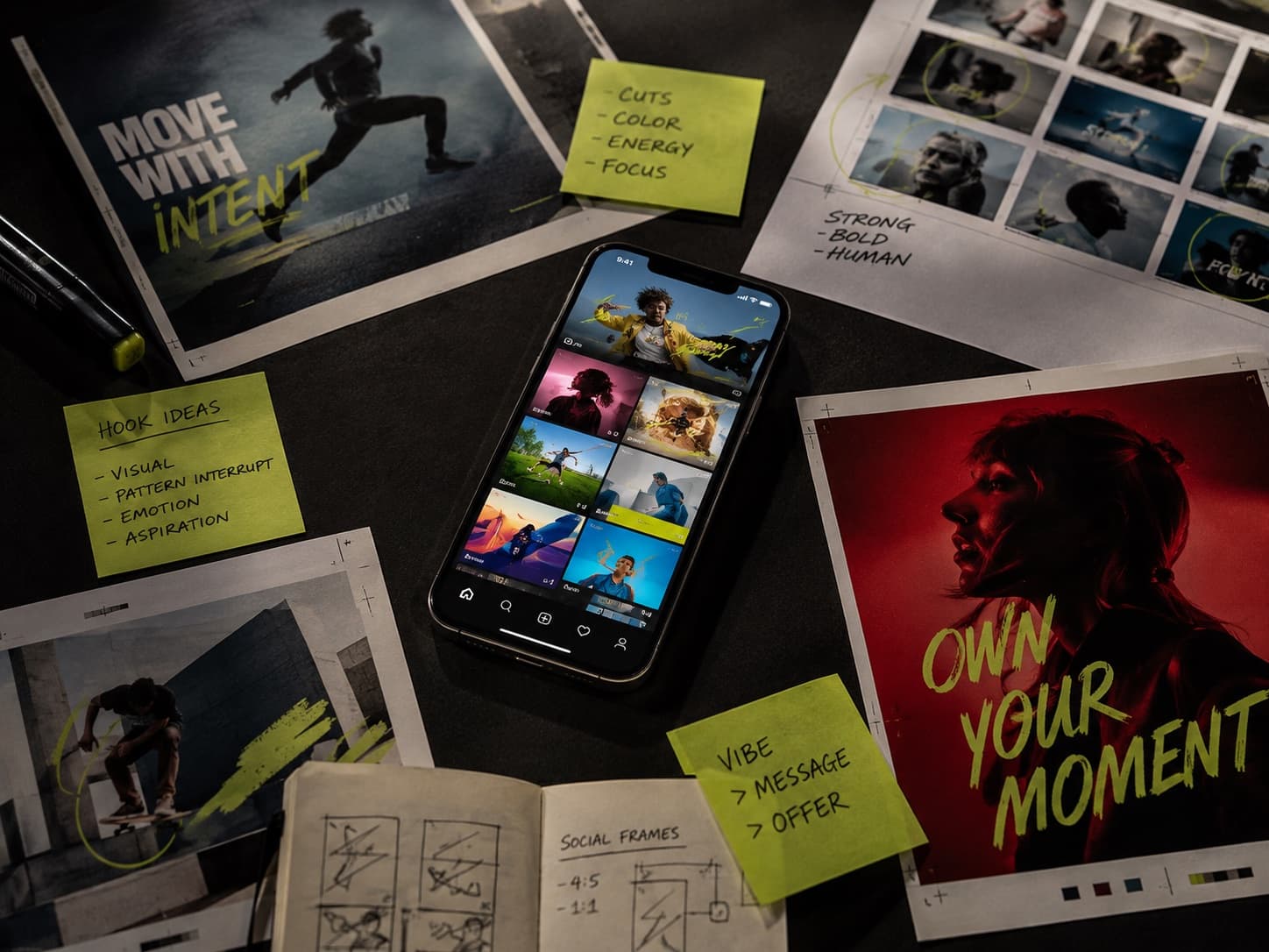 Campaign planning table with printed social ads, storyboards, and a phone showing a video feed